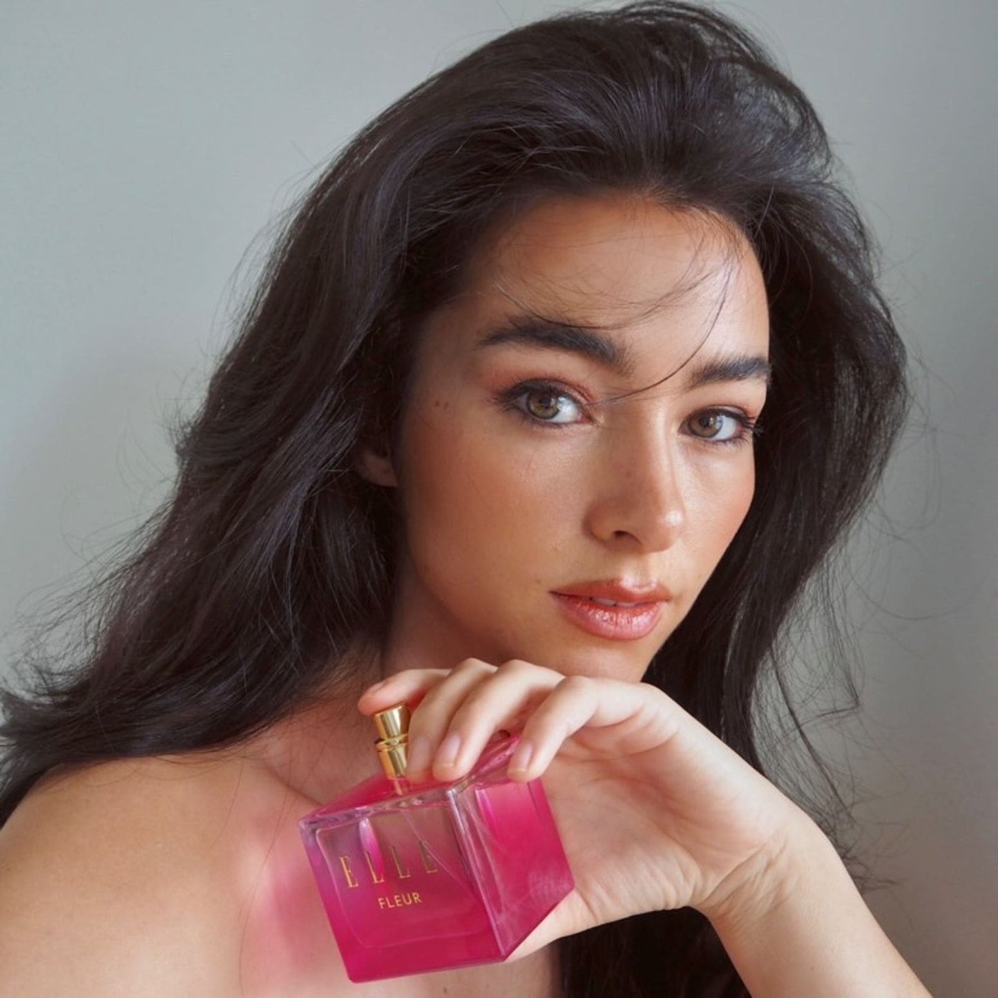 A female model holding Fleur fragrance by ELLE Parfums. A pink, girly bottle embodies a fruity, floral, and gourmand scent—perfect as an everyday eau de parfum for ladies and young women seeking a fresh, feminine fragrance.