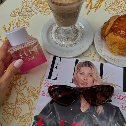 Lifestyle image of ELLE In Paris by ELLE Parfums and ELLE Magazine at a coffee shop in Paris. ELLE In Paris is a fruity and floral eau de parfum inspired by the elegant Parisian lifestyle. This versatile fragrance is ideal for both day and night, cruelty-free, and suitable for vegans and vegetarians. Perfect for those seeking a chic and ethical scent.