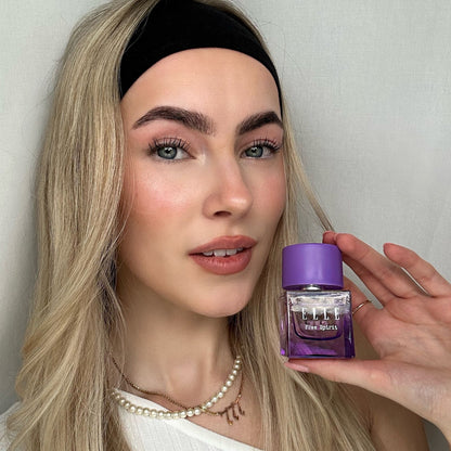 Model holding ELLE Free Spirit by ELLE Parfums, featuring a striking purple bottle with a feminine and captivating carton design. This fragrance embodies the celebration of individuality, the vibrancy of a free spirit, and the strength of womanhood. The eau de parfum offers a unique blend of woody and tropical notes, making it a bold and empowering choice.