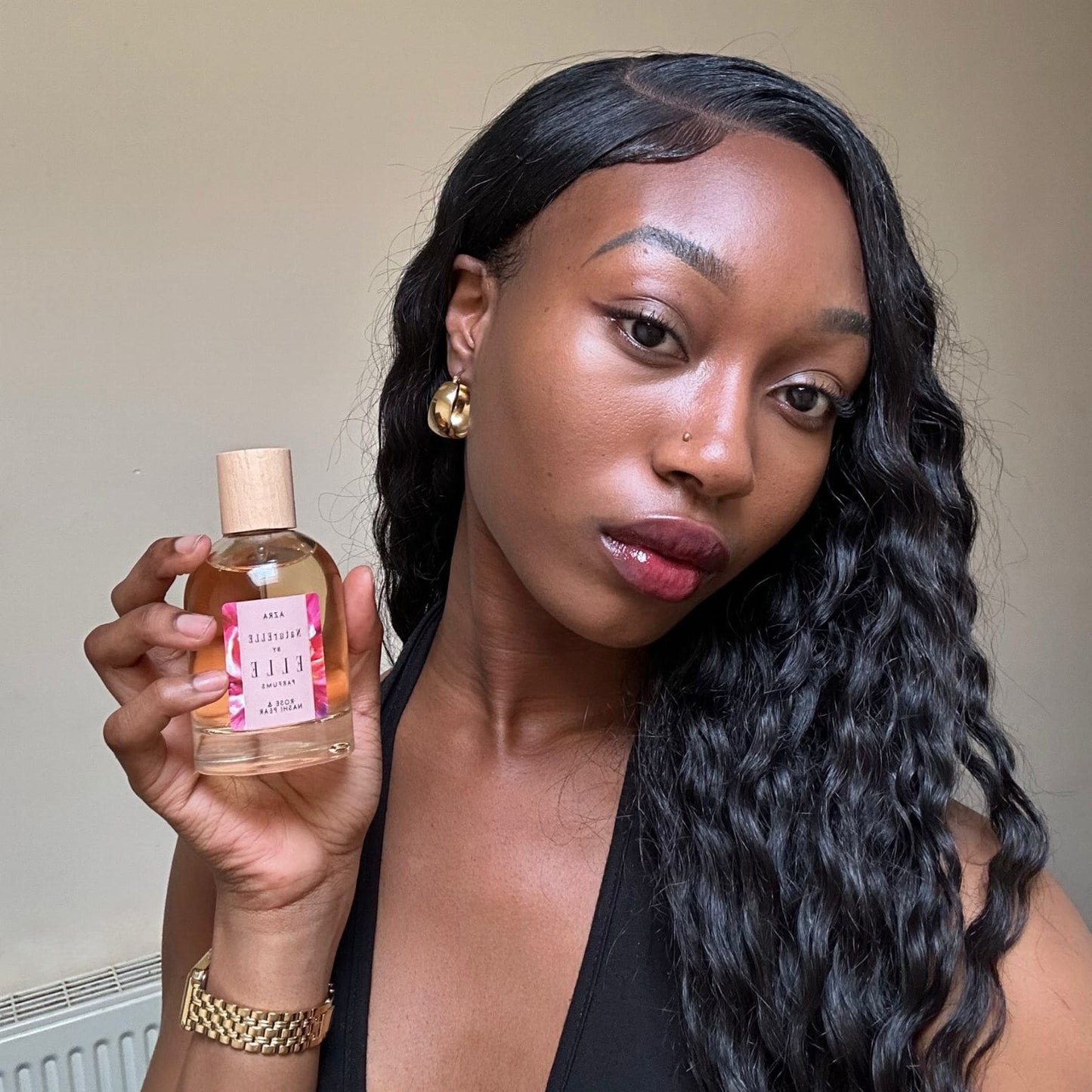 Image of a female model holding NaturELLE Azra by ELLE Parfums 100ml. The main ingredients in Azra Eau De Parfum are Rose & Nashi Pear. It's vegan, cruelty-free, naturally and ethically sourced. It's perfect for day and night.