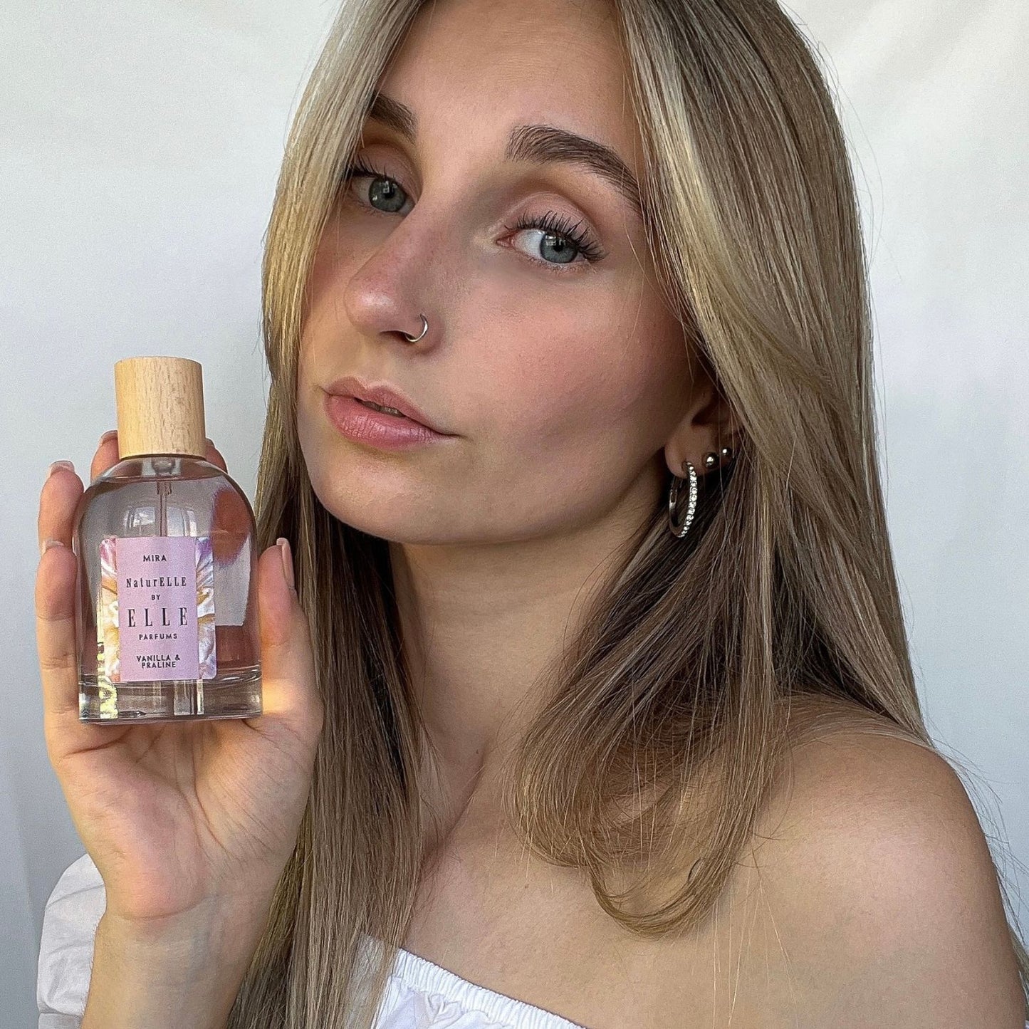 Image of a female model holding Mira by ELLE Parfums 100ml. The main ingredients in Mira Eau De Parfum are Vanilla & Praline. It's vegan, cruelty-free, naturally and ethically sourced. It's perfect for day and night.