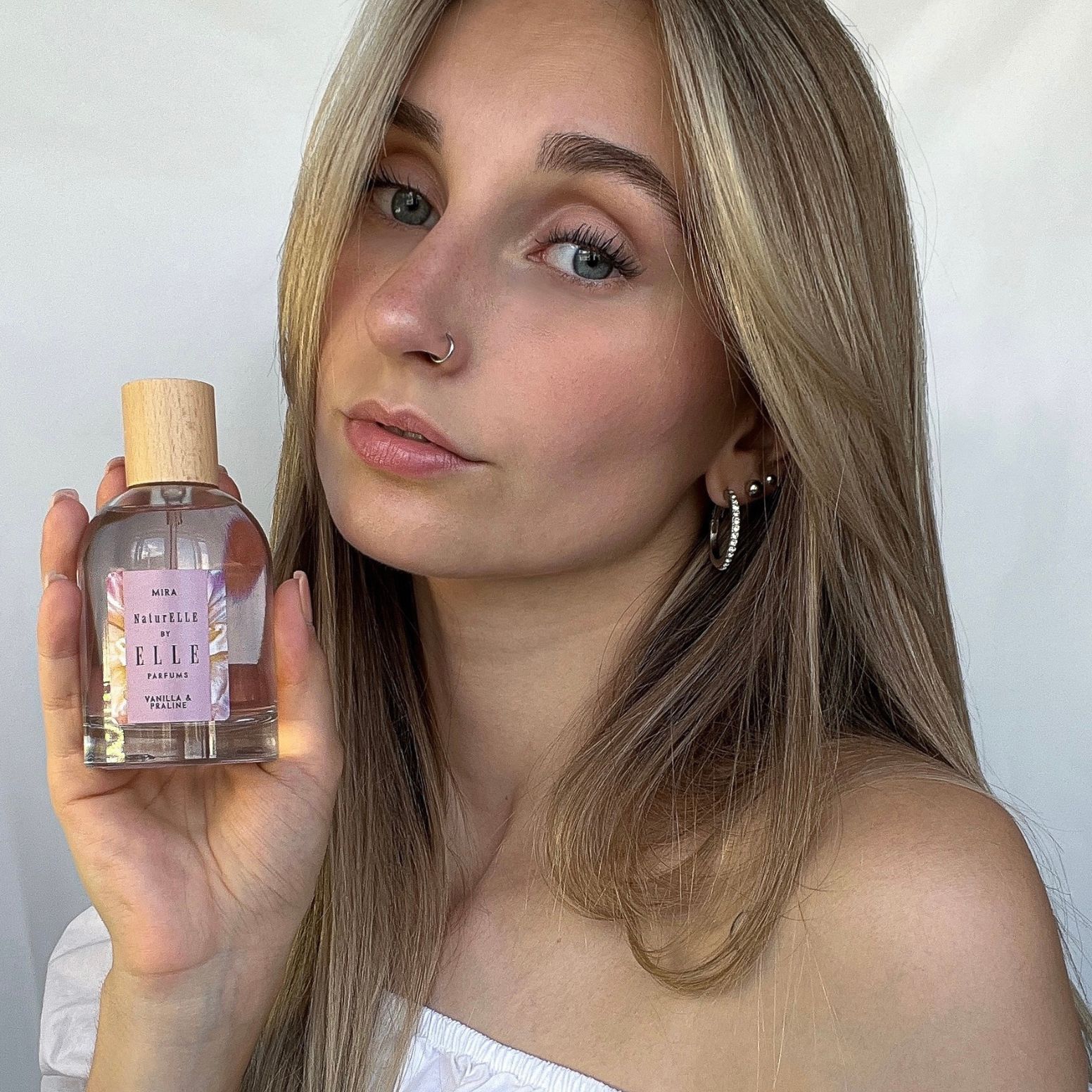 Image of a female model holding Mira by ELLE Parfums 100ml. The main ingredients in Mira Eau De Parfum are Vanilla & Praline. It's vegan, cruelty-free, naturally and ethically sourced. It's perfect for day and night.