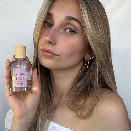 Image of a female model holding Mira by ELLE Parfums 100ml. The main ingredients in Mira Eau De Parfum are Vanilla & Praline. It's vegan, cruelty-free, naturally and ethically sourced. It's perfect for day and night.